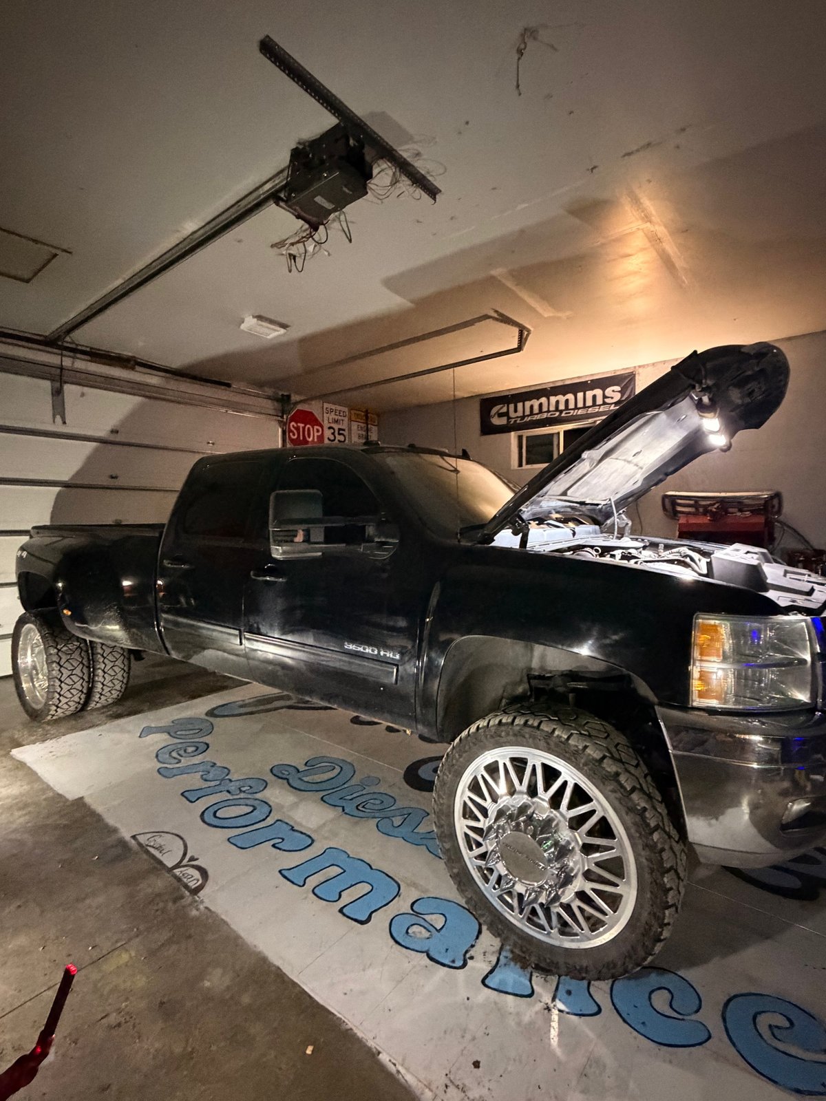 A black dually pickup in the shop with its hood open.