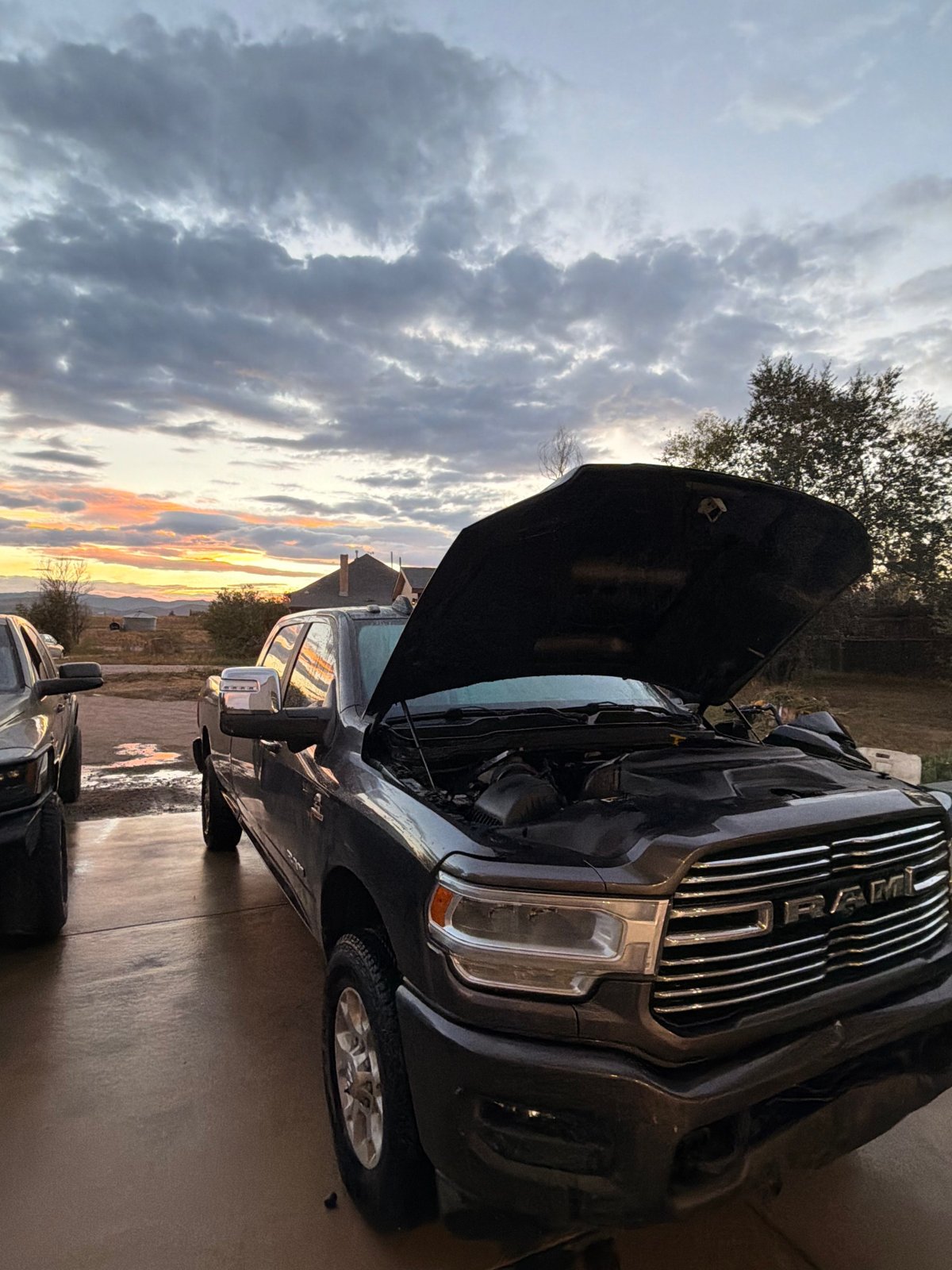 A Ram pickup with its hood open outside the shop at sunset.
